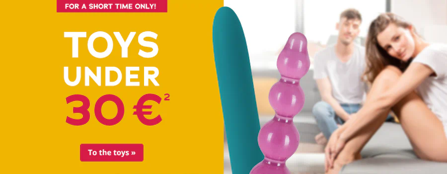 Advertisement with the text 'Toys under 30€'. The background is divided into two parts: Solid yellow behind the words, the other half shows a woman smiling and sitting on a bed in the foreground. A friendly looking man is sitting behind the woman. Two toys are in the foreground, a vibrator and an anal dildo. There is a call-to-action button at the bottom with the words 'To the toys »'.