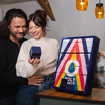 A couple stands in a cozy kitchen, opening a drawer of the ORION advent calendar. Both are smiling and look happy.